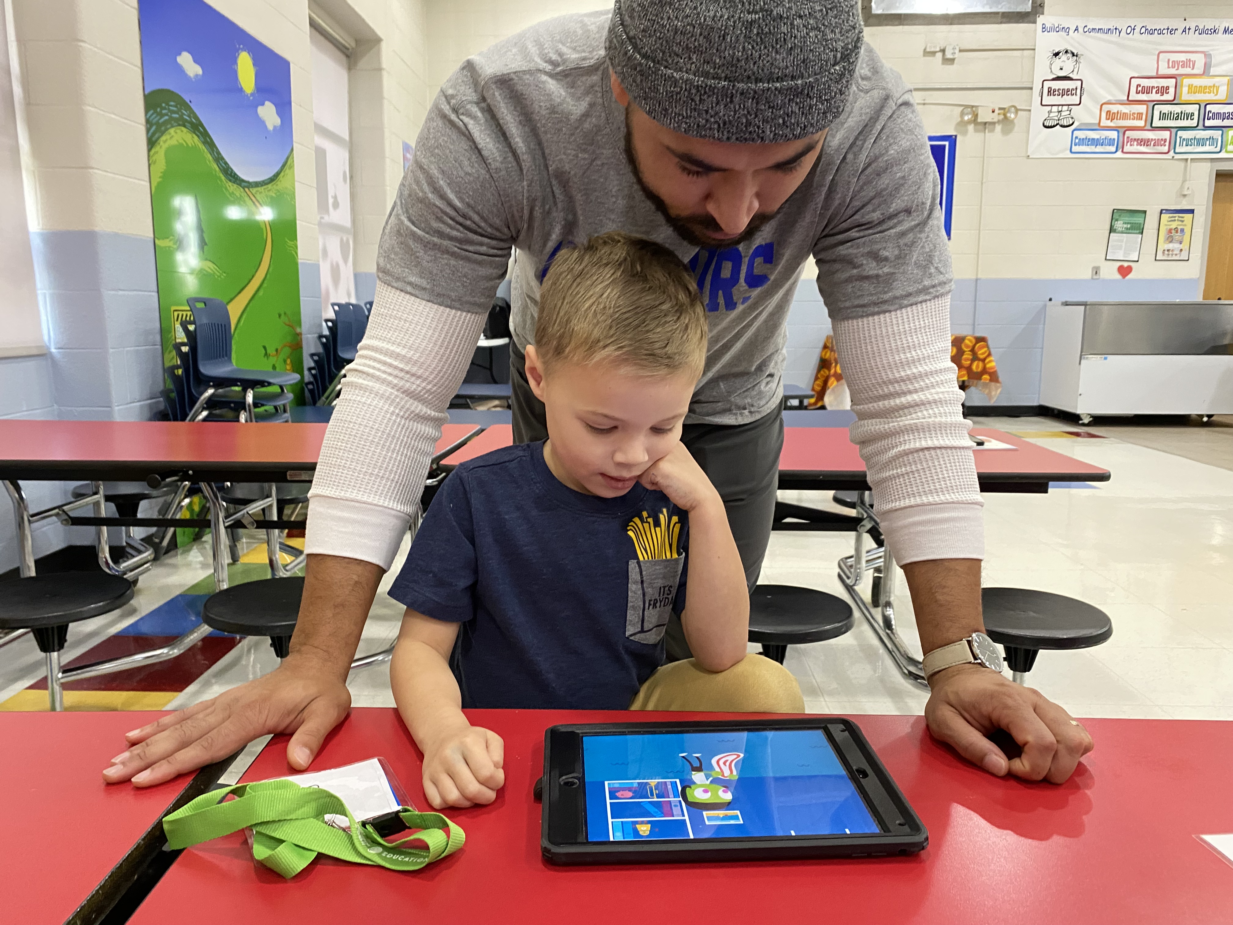 A man is looking over a child while they watch a show on an iPad.