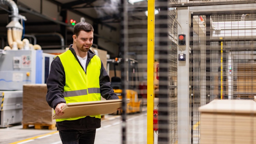 A white man with down syndrome carrying a piece of wood in a sheltered workshop