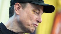 Elon Musk wearing a black baseball cap with a black eye, looking smugly to the left