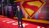 James Gunn stands on a red carpet in front of a Superman logo