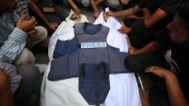 Mourners gather around two bodies of journalists killed Sunday in Gaza. The bodies are wrapped in white sheets and a press vest lays on top of them.