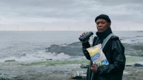 A Black man holding a bag of chips by the seaside.