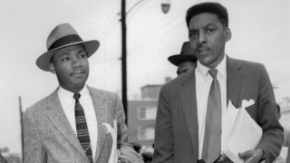 A black-and-white photograph of two middle-aged African American men in suits and ties walking side by side down a city sidewalk.