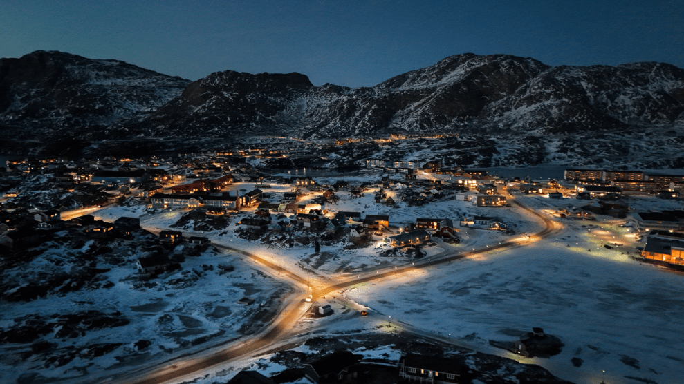 An aerial view shows a small city in a snowy, dark valley.