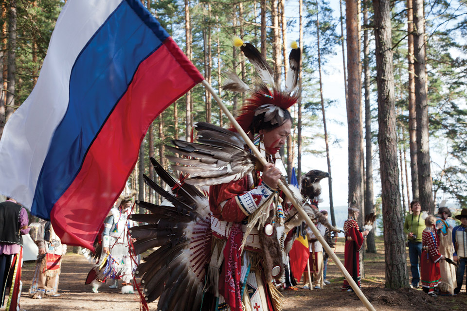 Man dressed as Native America carring a flag.